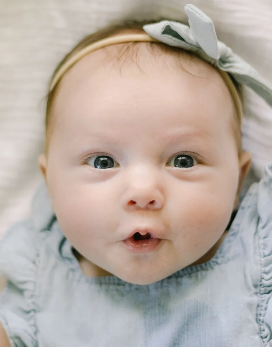 Close-up of a wide-eyed baby girl in a blue headband during an in-home milestone session