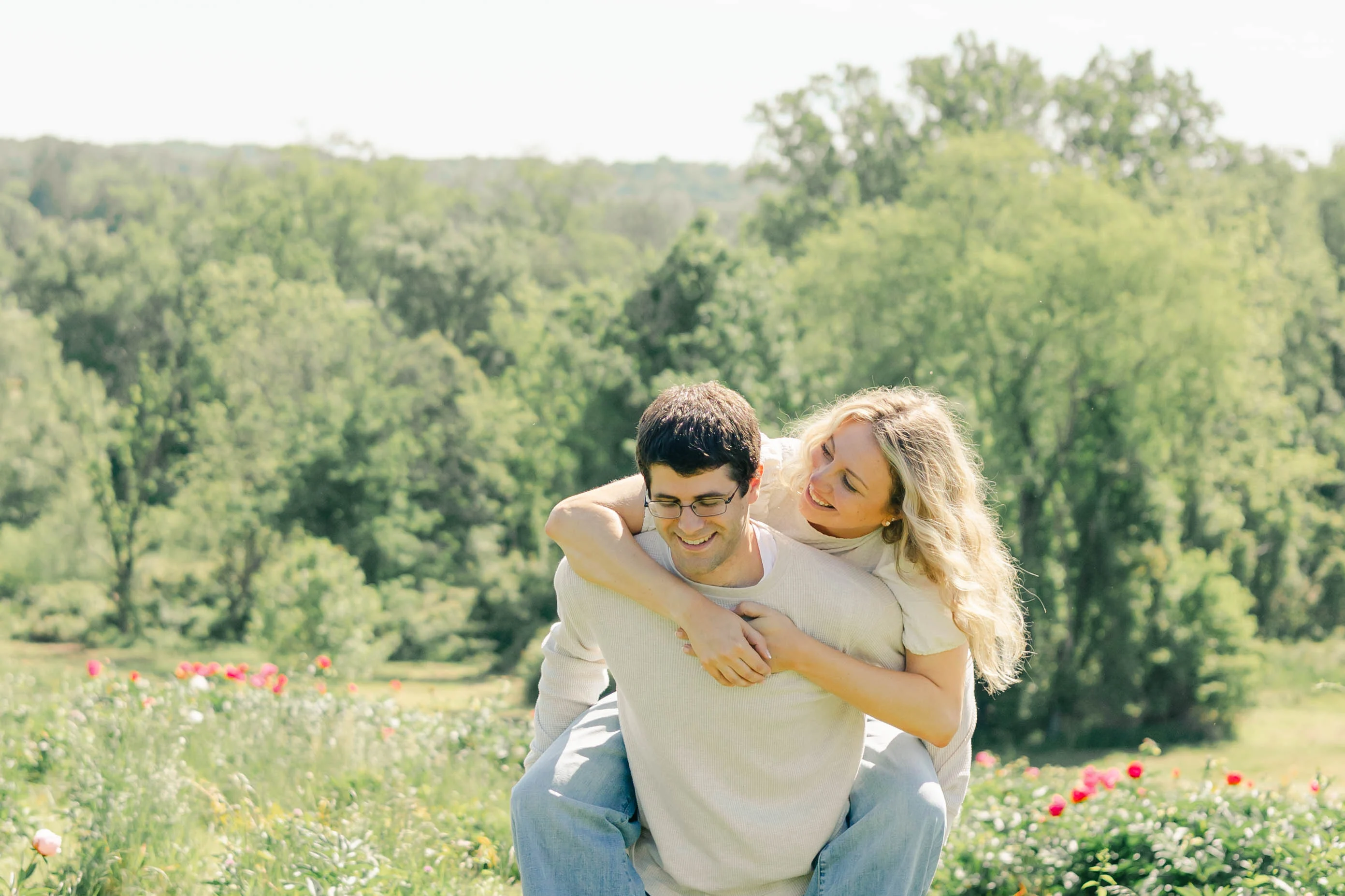 Laughing couple sharing a piggyback hug above a green wooded valley in summer