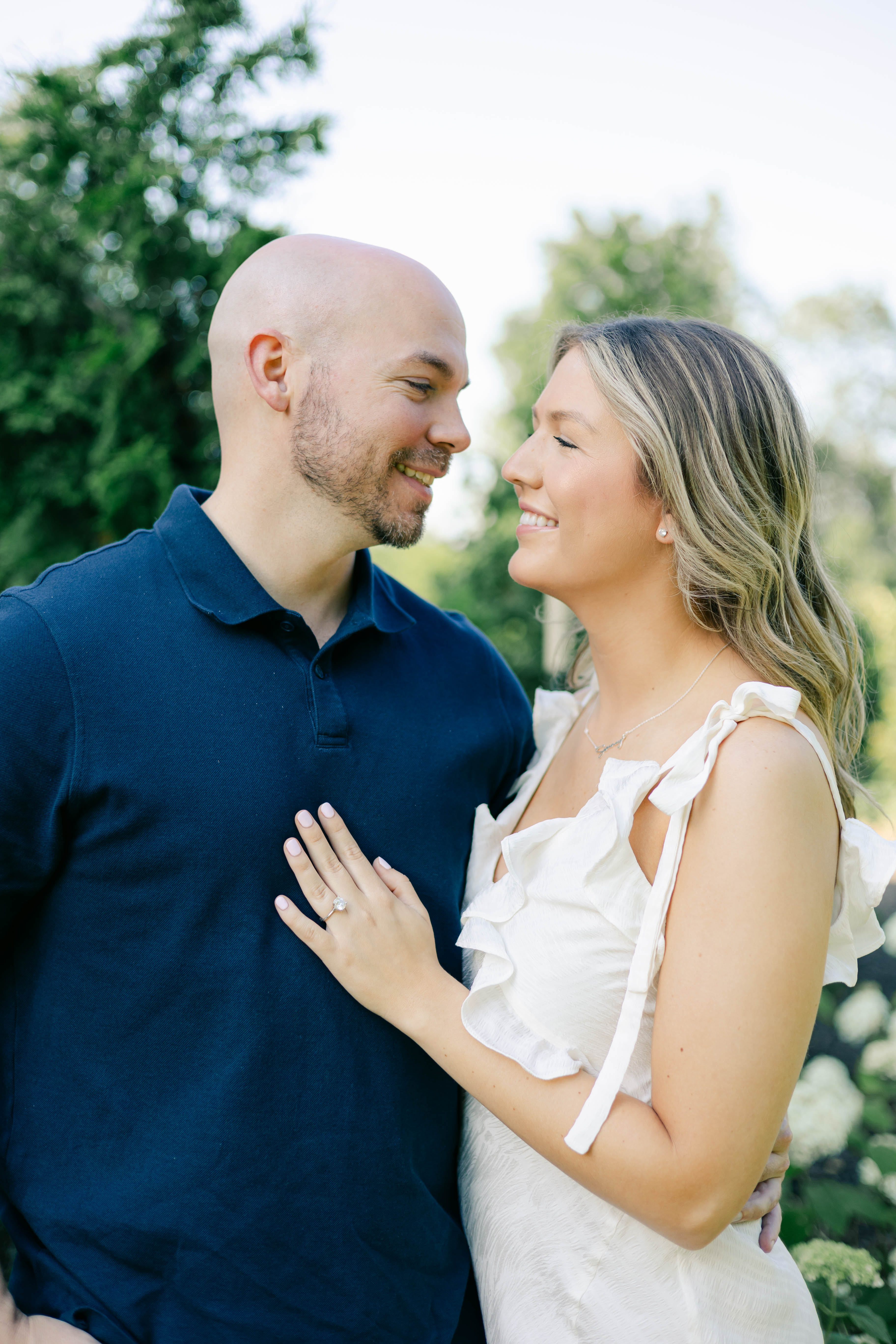 Couple smiling at each other in a summer garden, her hand with an engagement ring on his chest