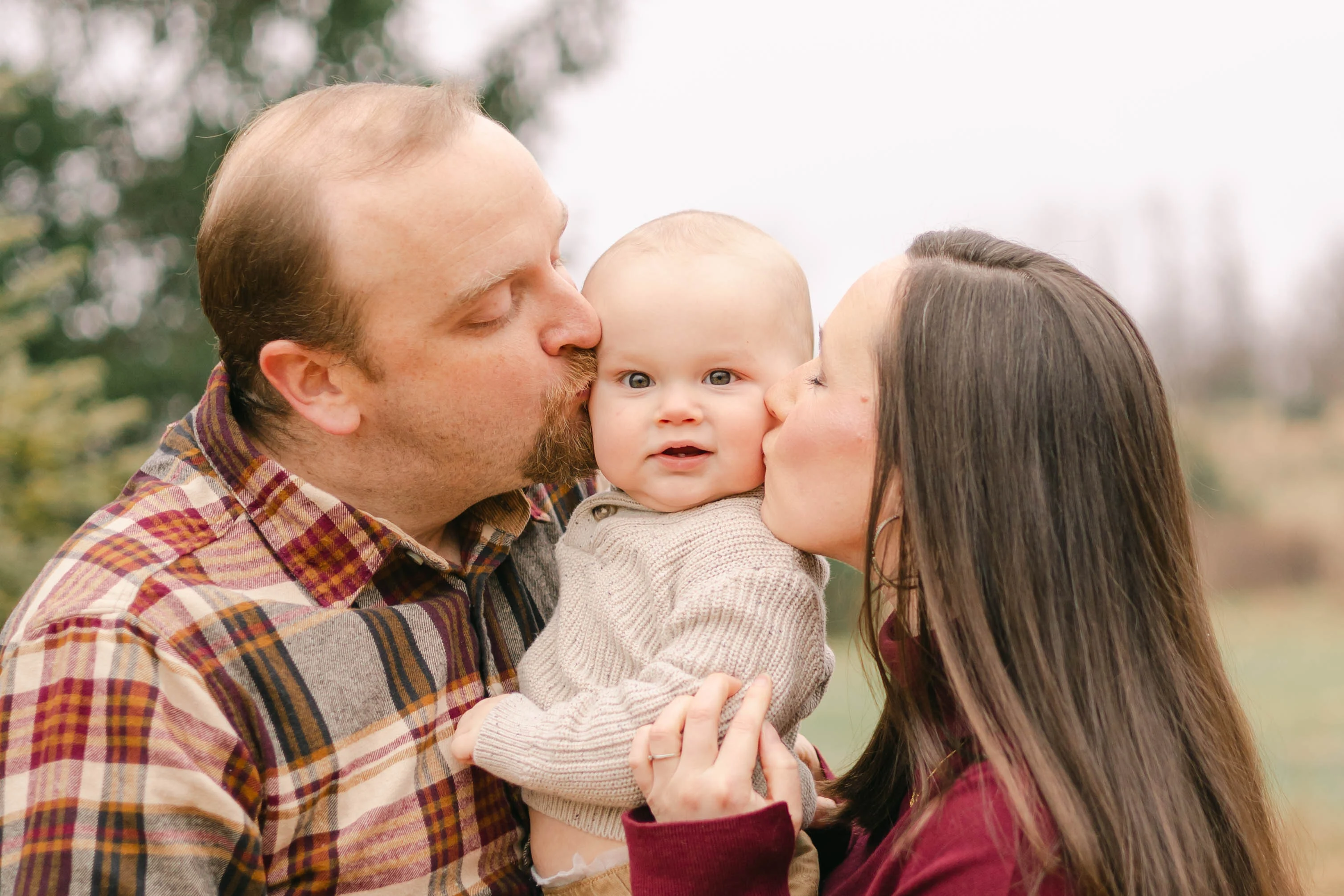 Mom and dad kissing their baby's cheeks during a fall family session