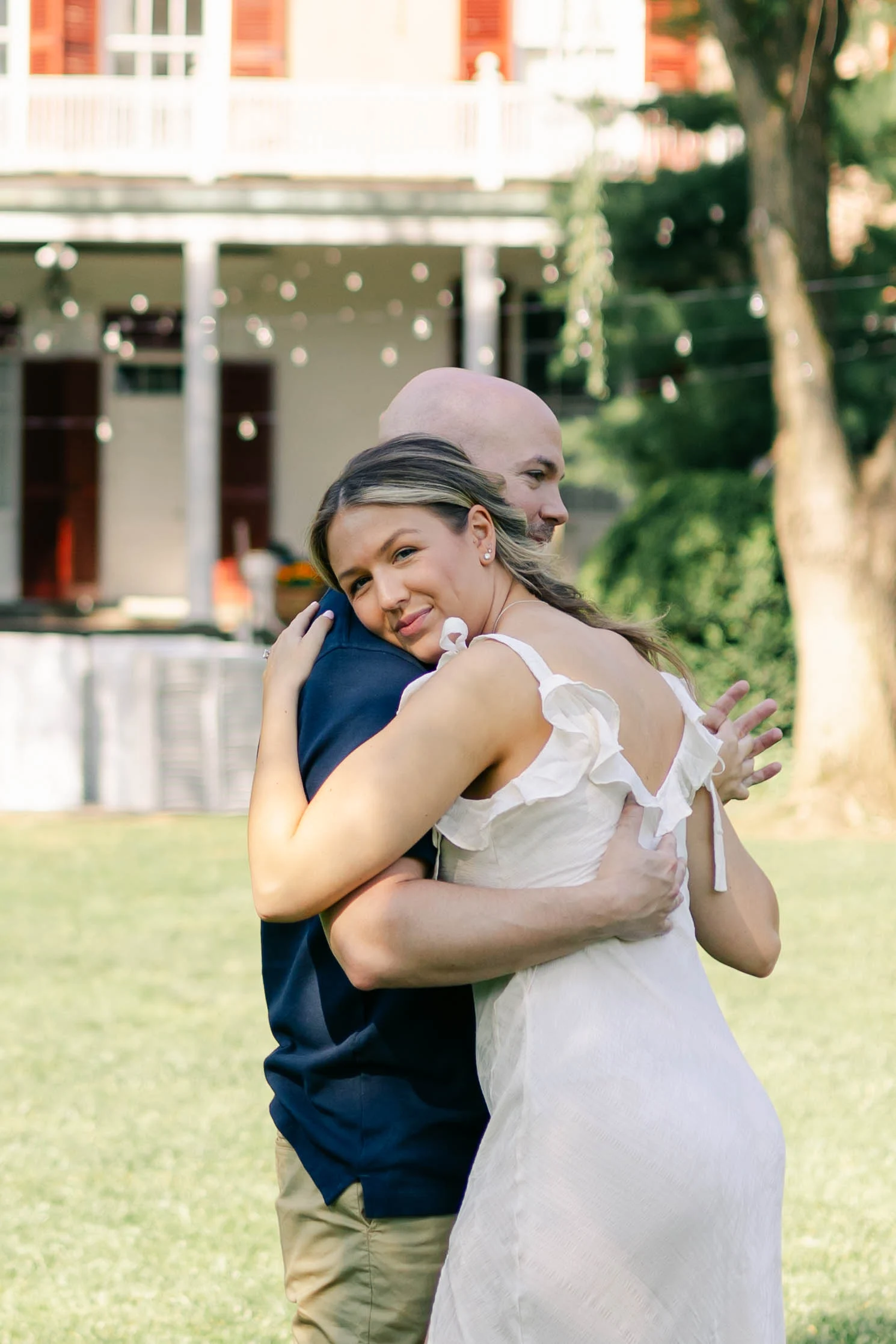 Couple embracing on the lawn in front of a historic white farmhouse